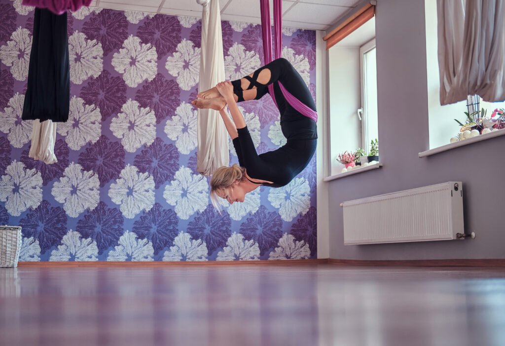 young woman doing aerial yoga practice in purple hammock in fitness club.